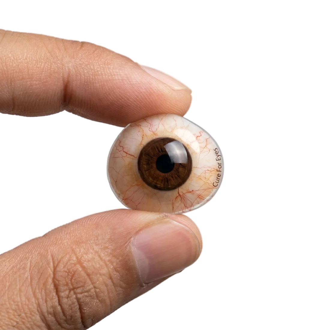 Custom hand-painted ocular prosthesis (artificial eye) crafted at Cure For Eyes Gurugram, held between fingertips to show realistic hand-painted iris, scleral tone and vasculature in medical-grade PMMA.